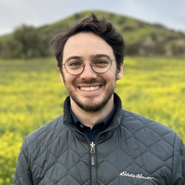 Micha’el Miller, a therapist in Colorado, smiling outdoors in a field of wildflowers.