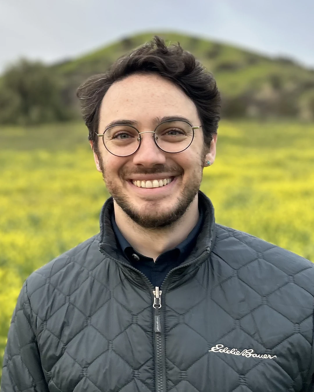 Micha’el Miller, smiling outdoors in a field of yellow wildflowers.
