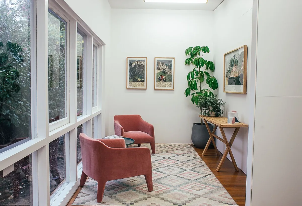 A calm consulting room with two armchairs facing each other, a plant, and windows opening to greenery.